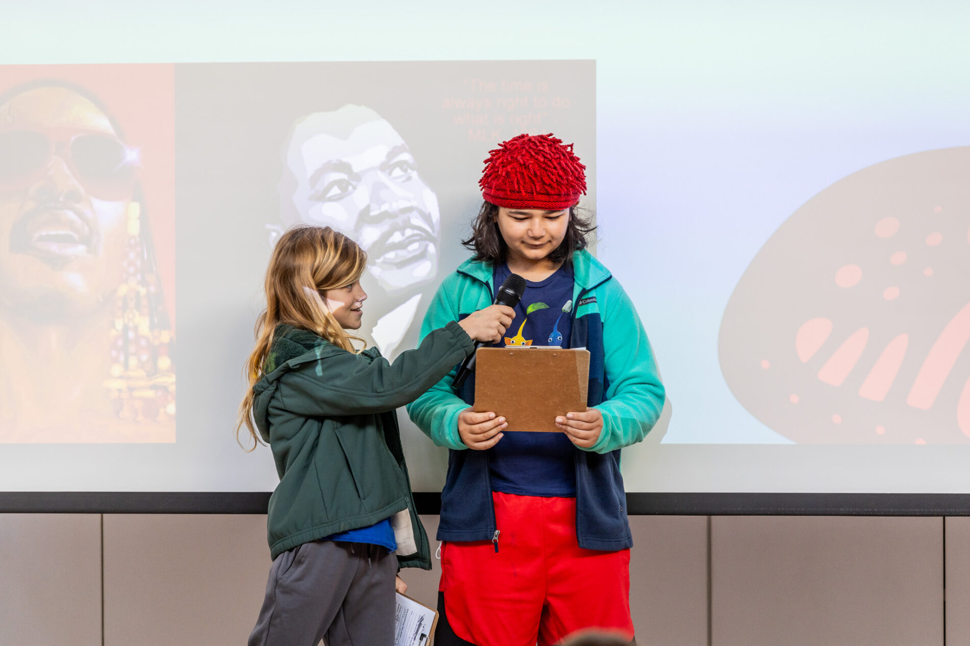 A student holds a microphone up to another student as they present on Martin Luther King Junior Day.
