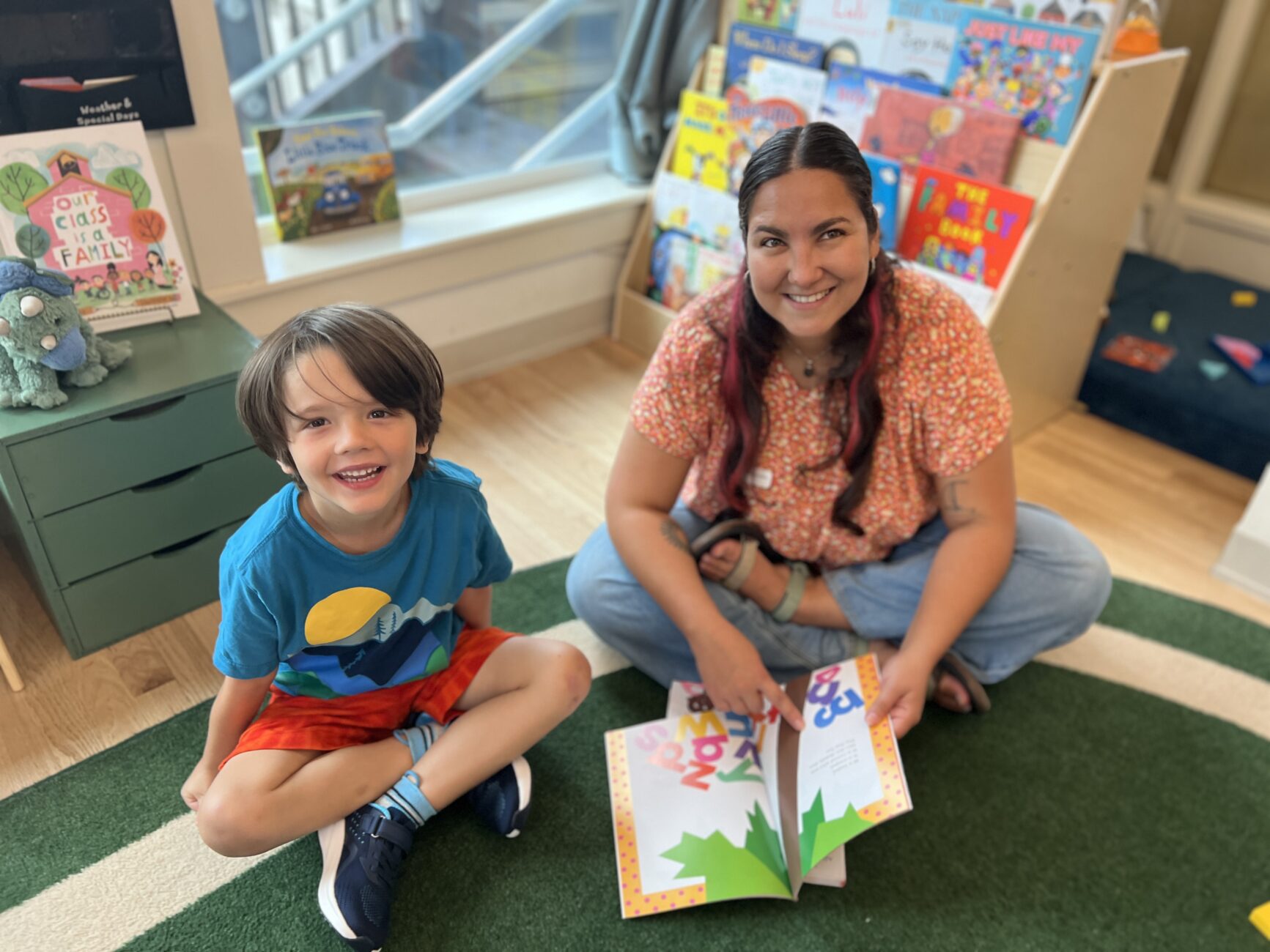 A teacher and student look up, smiling, from reading a book together.