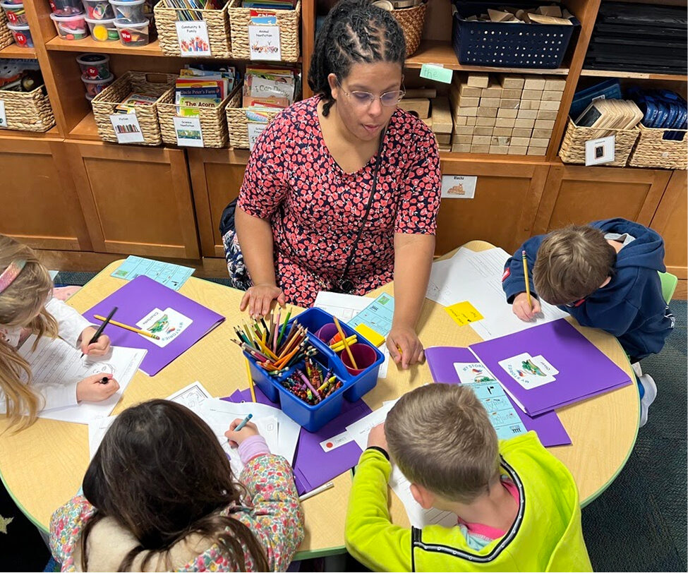 students coloring with teacher at desk